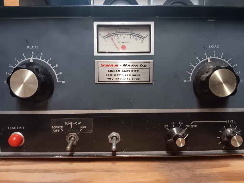 Front panel of Swan-Mark 6B linear amplifier showing plate and load knobs and a central meter (RF power/readout) with a metal badge below reading 'Swan-Mark 6B Linear Amplifier'.