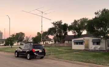 VHF Grid Activation — DM86 in Stratford Texas Black SUV parked on a residential street at sunset with a small house, trees, and a tall TV antenna nearby.